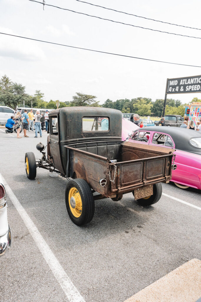 Weathered custom pickup with an open bed and yellow wheels at a vehicle gathering.