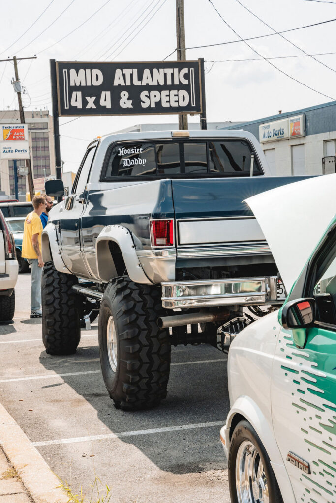 Lifted blue-and-white pickup with oversized tires beneath the Mid Atlantic 4x4 & Speed sign.