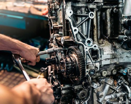 Mechanic using hand tools on an exposed engine assembly.